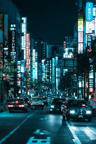 vehicles on roadway between lighted buildings at night