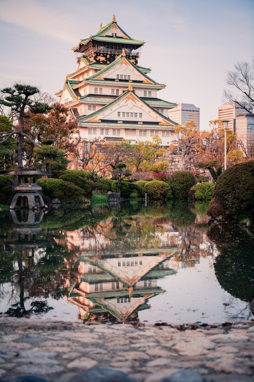 white, green and gold temple surrounded by trees near lake during daytime